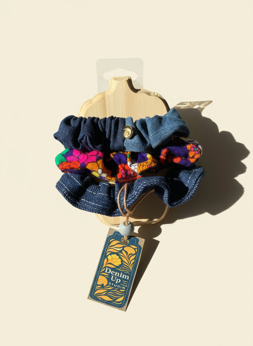 Set of colorful scrunchies with a denim scrunchie on a wooden surface, featuring a brand tag.